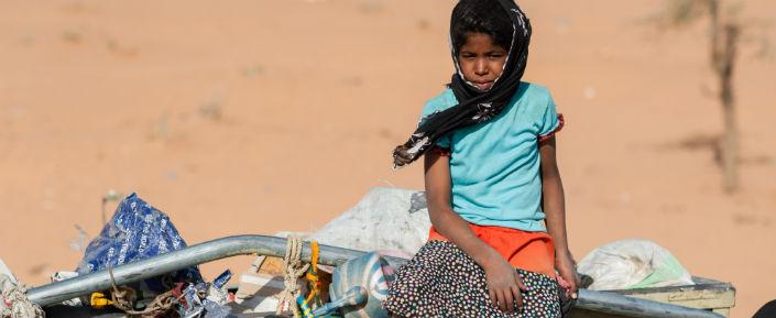 Ein Mädchen sitzt auf einem mit Flüchtlingen und deren Habseligkeiten beladenen LKW.