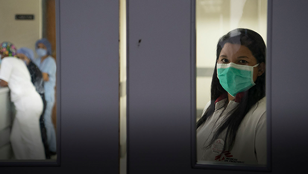 Sozialarbeiterin Dulce Herrera mit Mundschutz auf steht hinter Glastür einer Krankenhausstation in Caracas