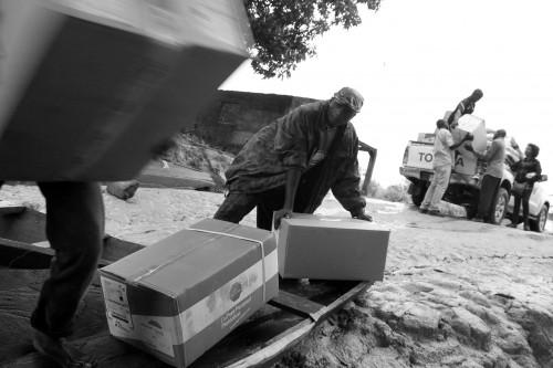MSF-Mitarbeiter aus Guinea und  Piroge-Steuermänner schlichten Boxen mit PPE (Personal Protection Equiment) in die Piroge, um sie über den Makona-Fluss nach Liberia zu bringen. © Martin Zinggl