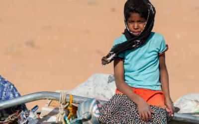 Ein Mädchen sitzt auf einem mit Flüchtlingen und deren Habseligkeiten beladenen LKW.