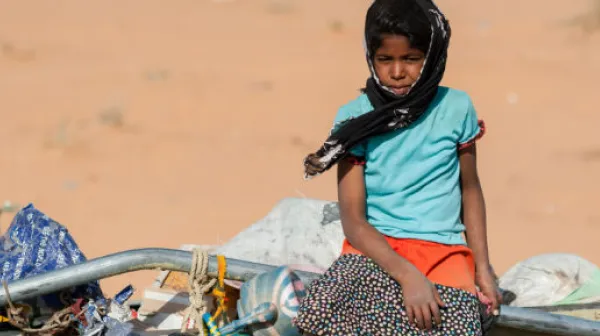 Ein Mädchen sitzt auf einem mit Flüchtlingen und deren Habseligkeiten beladenen LKW.
